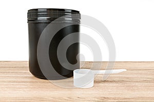 Black supplement tub with scoop on a wood patterned background