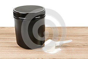 Black supplement tub with scoop on a wood patterned background