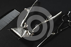 On a black surface are old barber tools. vintage manual hair clipper, comb, hairdressing scissors. black monochrome