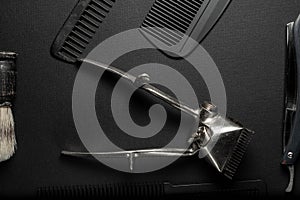 On a black surface are old hairdresser tools. vintage hand-held hair clipper, hairdressing scissors, combs, razor, shaving brush.