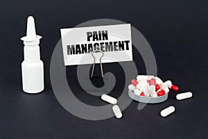 On a black surface are pills, a nasal spray and a paper sign with the inscription - Pain management