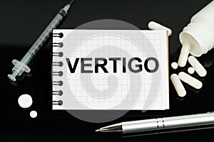 On the black surface are pills, a syringe and a notebook with the inscription - vertigo