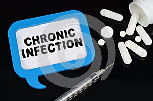 On a black surface, a syringe, pills and a blue frame with the inscription - chronic infection