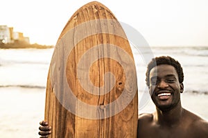 Black surfer man holding vintage surf board on the beach at sunset - Focus on face