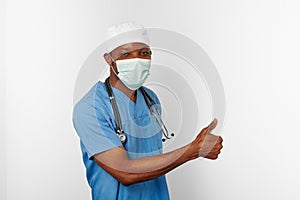 Black surgeon doctor man in blue coat white cap and surgeon mask with thumbs up gesture