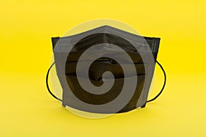 Black surgical mask for protection against Coronavirus COVID-19 and other contagious diseases. Isolated on yellow background