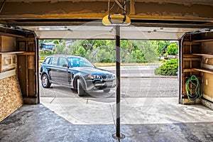 Black Suv turning into garage with automatic overhead door opener - grainy unfinished surfaces and pavement - Suburban