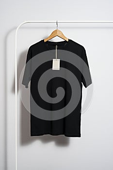 Black t-shirt mockup with blank price tag on wooden hanger hanging on a clothes rack