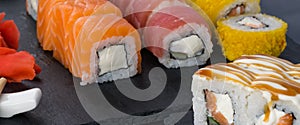 On a black table, a close-up of assorted Japanese rolls of salmon, tuna and baked in tempura