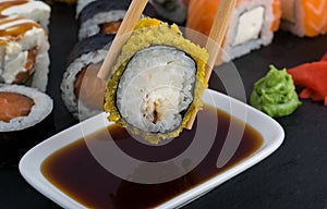 On a black table, close-up, baked roll in tempura, wooden sticks are lowered into a container with soy sauce, against a background