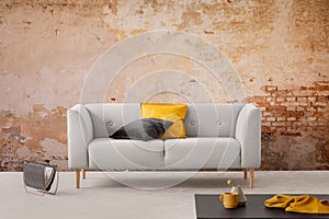 Black table and grey sofa with cushions in simple living room interior with red brick wall. Real photo