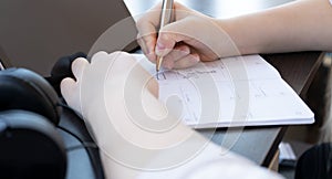  black tablet, black headphones, white hands holding a pen, writing on a white sheet, learning remotely, onli