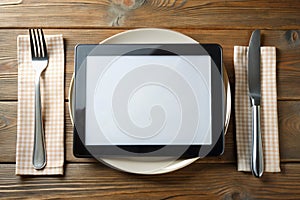 Black tablet PC on dinner table with plate, fork, and knife
