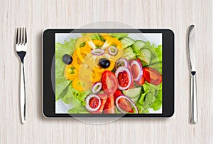 Black tablet pc with healthy food on screen and wooden table