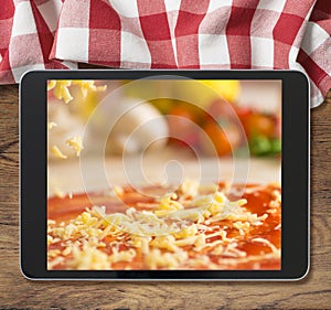 Black tablet pc with pizza displayed on wooden table and picnic tablecloth