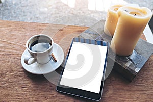 Black tablet with white blank desktop screen and coffee cup , book , candles on vintage wooden table in cafe