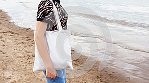 black tanned girl holding tote eco bag close up canvas fabric for mockup. young woman stands against of sand coast