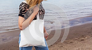 black tanned girl holding tote eco bag close up canvas fabric for mockup. young woman stands against of sand coast