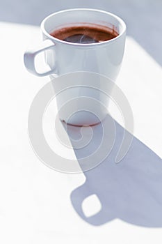 Black tasty coffee in white cup on white surface with shadow