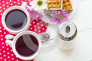 Black tea ceremony - a cup of tea, teapot, sugar, cakes, flowers on a red with white dots background