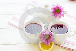 Black tea ceremony - a cup of tea, teapot, sugar, cakes, flowers on white wooden rustic background