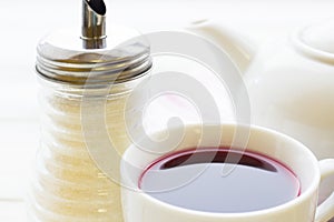 Black tea ceremony - a cup of tea, teapot, sugar, cakes, flowers on white wooden rustic background