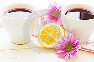 Black tea ceremony - a cup of tea, teapot, sugar, cakes, flowers on white wooden rustic background