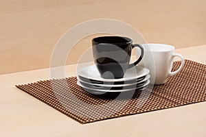 Black tea cup on the stack of the white and black plates near white tea cup on tablemat.