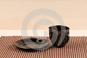 Black tea cup standing near black plate on tablemat.