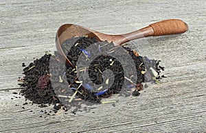 Black tea with dried fruits and petals in wooden spoon on wooden table
