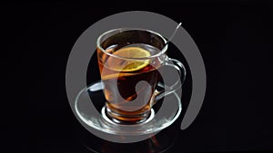 Black tea with lemon in glass tea Cup with saucer on black background