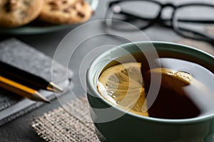 Black tea with lemon slices on a napkin of burlap with notepad pen, a pencil a plate of cookies and glasses