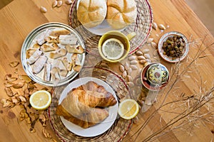 Black tea with lemon in yellow mug with croissants, buns and homemade cookies