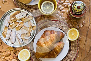 Black tea with lemon in yellow mug with croissants, buns and homemade cookies