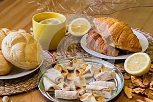 Black tea with lemon in yellow mug with croissants, buns and homemade cookies