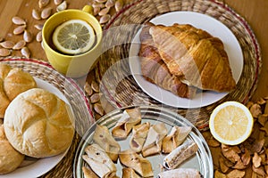 Black tea with lemon in yellow mug with croissants, buns and homemade cookies