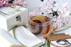 Black tea mug, open book, pink hydrangea flowers, cinnamon sticks, spoon, casket