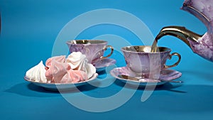 Black tea is poured into beautiful pink porcelain cups on a blue background. There is a saucer of marshmallows next to