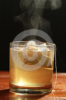 Black tea with tea bag in glass and with steam Vapour - macro view with black background photo