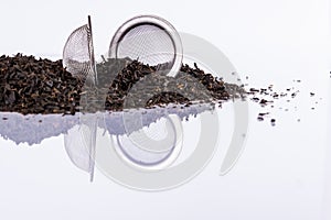 Black tea and tea strainer on white background.