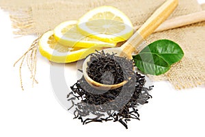 Black tea in wooden spoon and green lemon leaves.