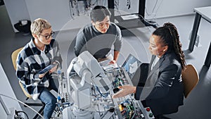 Black Teacher with Laptop and Two Diverse Students Analyse and Discuss Futuristic Robotic Arm During