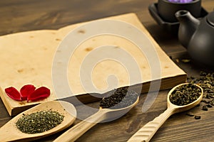 Black teapot, cups, tea collection, flowers, old blank open book on wooden background. Menu, recipe