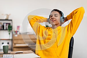 Black teen guy relaxing with music, hands behind head, wearing headphones