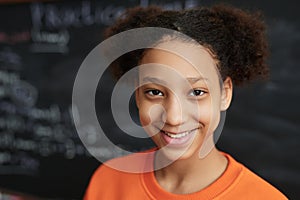 Black teenage girl by blackboard in school classroom smiling at camera