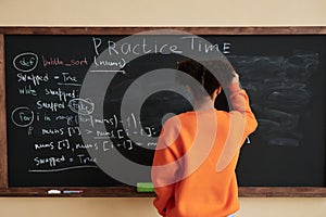 Of black teenage girl writing on blackboard in school classroom