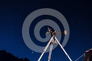 Black telescope reflector on a tripod under the starry dark blue night sky