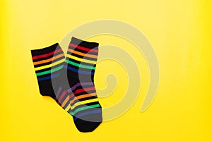 Black textile cotton socks with striped bright colorful pattern over yellow background