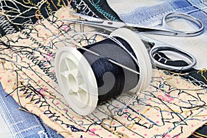 Black thread with a needle on a plastic spool and scissors on the work table of a tailor