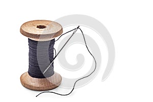 Black thread on an old wooden spool and sewing needle